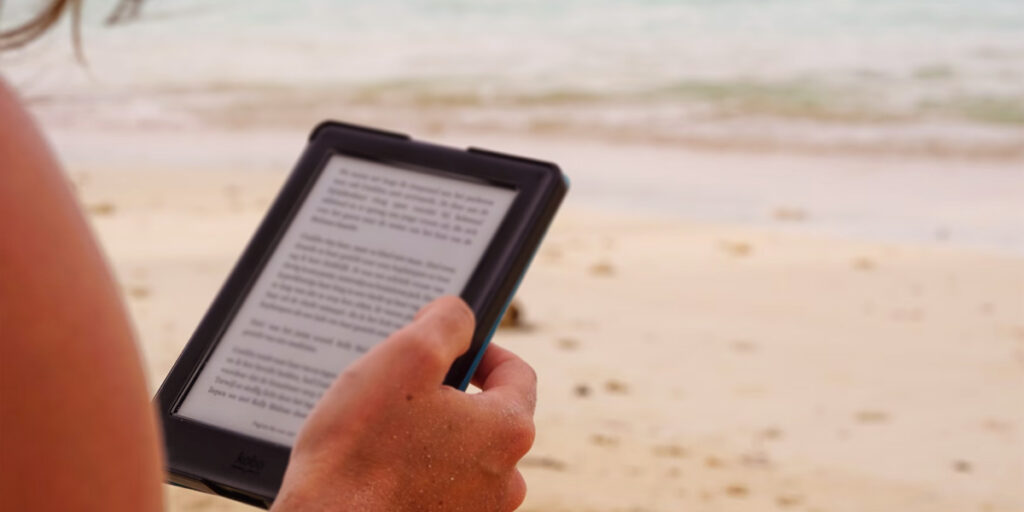 Person reading an e-reader on a beach