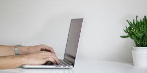Hands writing on a laptop next to a plant