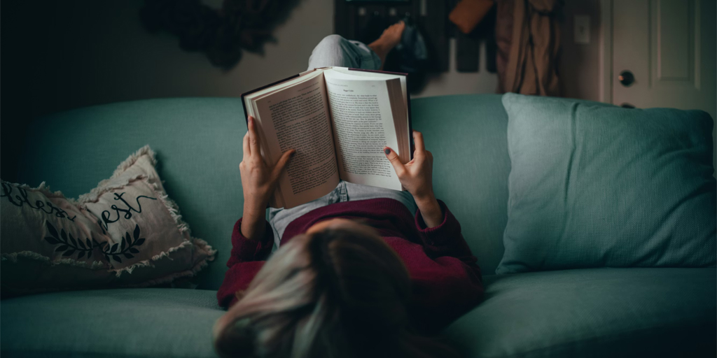 A woman lying upside down on a sofa, reading a book